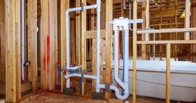 Open wall framing with new PVC drain and vent piping roughed in beside a tub
